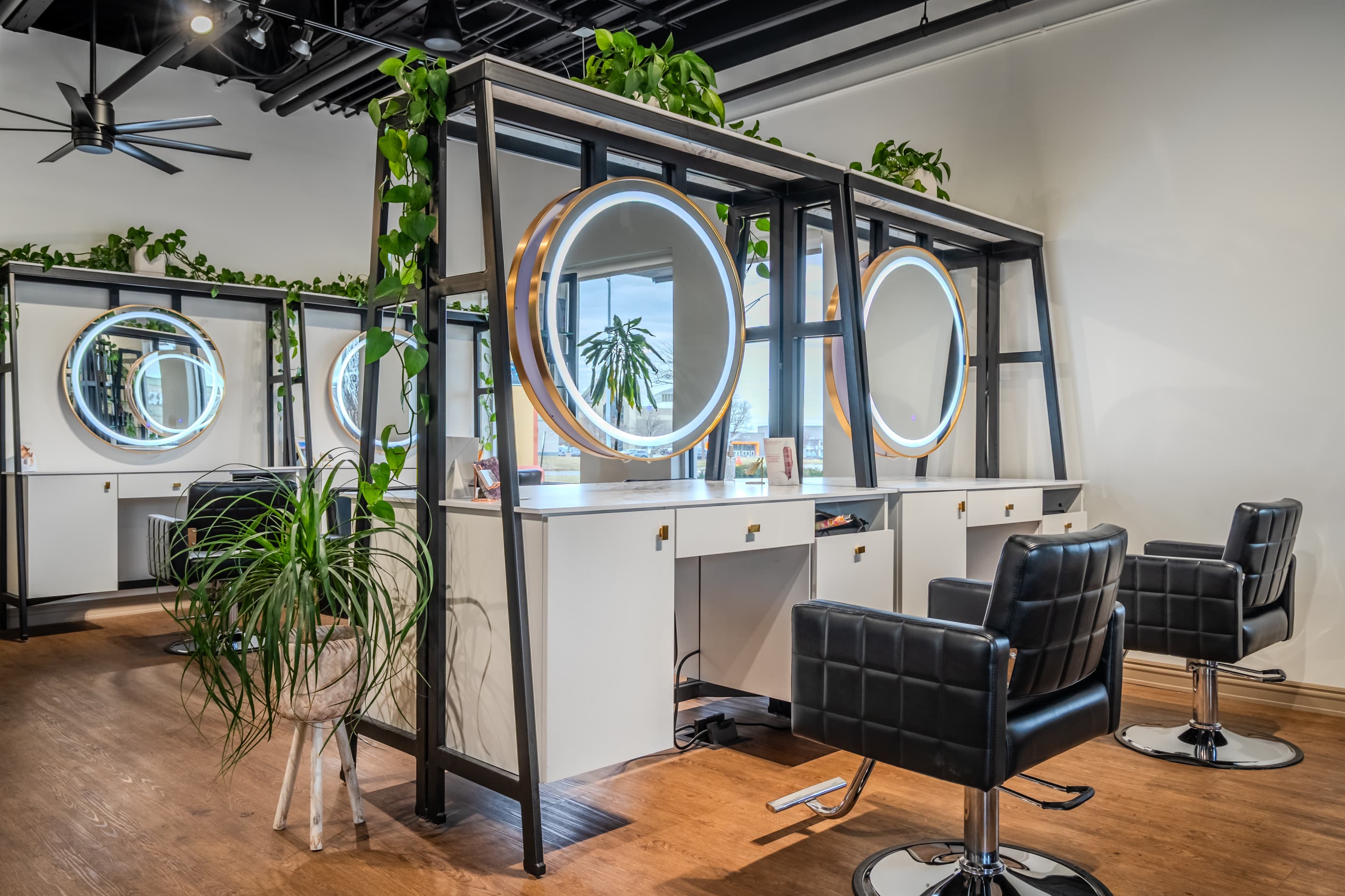 Plant-lined styling stations with illuminated round mirrors at Reveal Salon & Spa